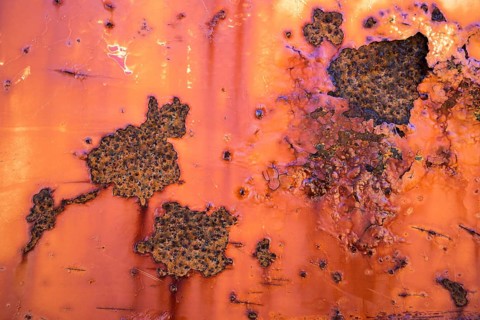 Peeling paint and rust on orange metal wall