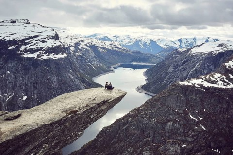 Paar sits on a rock platform on Trolltunga and looks over fjord landscape