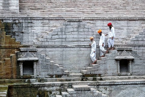 Three indian men walking down the steps at the stepwell Toorji Ka Jhalra in Jodhpur