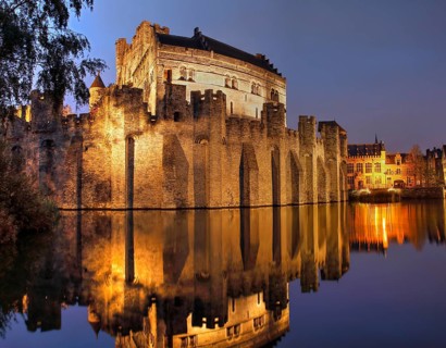 Illuminated castle Gravensteen at dusk with water reflection
