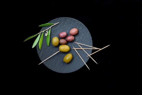 Green and black olives with toothpick on black plate