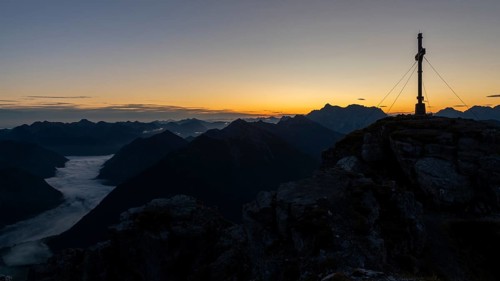 Sunrise with cross of the Thanell summit and Lechtal Alps with fog in the valley