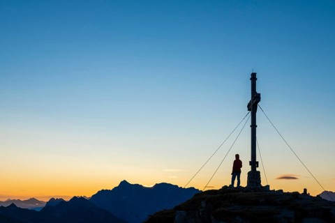 Sunrise with cross of the Thanell summit and mountaineers with Lechtaler Alps