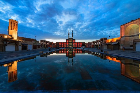 Amir Chaqmaq complex facade illuminated at sunrise and reflecting in a pond