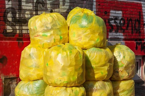Stacked yellow bags for plastic waste in front of a house wall