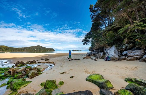 Young woman standing on beach with moss-covered rocks