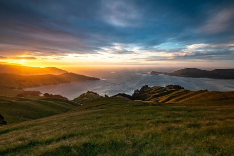 View of meadows and rocky coast at sunset