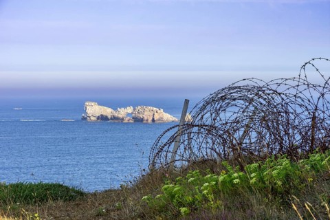 Barbed wire and view of small island in the sea