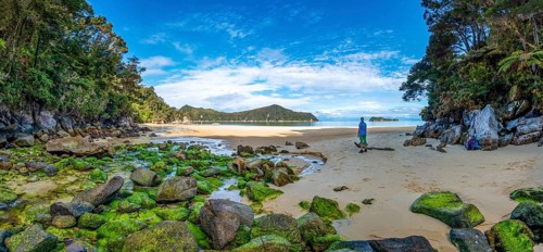 Young woman standing on beach with moss-covered rocks