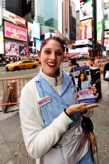 Young woman in waitress costume and cupcakes on her head promoting a musical