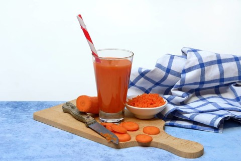 Carrot juice in glass and carrot slices on wooden board