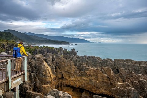 Young man on viewing platform looking over coastal landscape with sandstone rocks