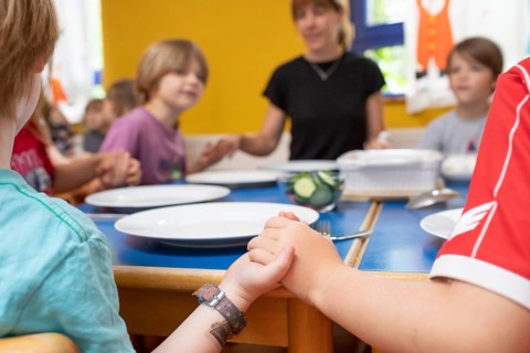 Children and nursery school teacher in the dining room of the kindergarten hold hands and speak a table motto