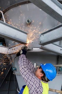 Construction worker processes a steel beam with an angle grinder on a large construction site