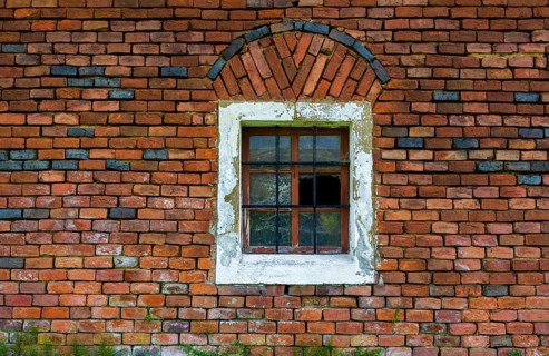 Wall of red bricks with barred stable window and broken panes