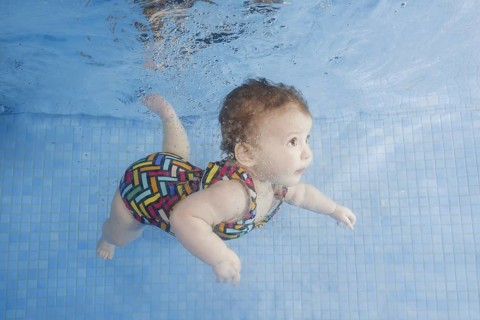 Little baby in a swimsuit learning to swim underwater in a swimming pool