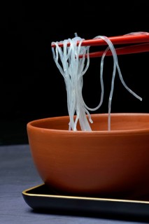 Asian glass noodles on chopsticks over bowl