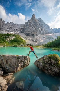 Hiker jumps from stone to stone at the turquoise green Sorapis lake