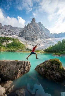 Hiker jumps from stone to stone at the turquoise-green Sorapis lake