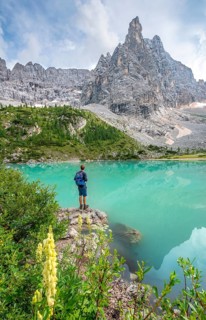 Young man hiker at the turquoise-green Sorapis lake with flowers