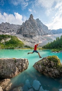 Hiker jumps from stone to stone at the turquoise green Sorapis lake