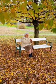 Senior citizen sitting on a park bench in autumn