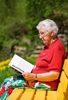 Senior sitting on a garden bench reading a book