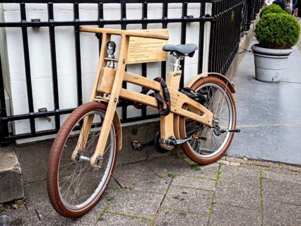 Wooden bicycle chained to an iron fence