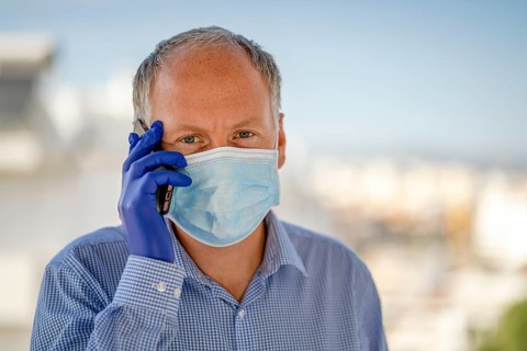 Man using protective mask and blue latex gloves while using mobile phone