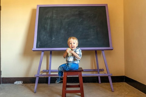 Friendly blonde boy sitting with a blackboard sponge by an empty blackboard