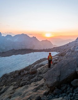 Hiker stands in rocky alpine terrain and looks at sunset over Gosaukamm with mountain peak Bischofsmuetze