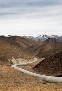 Barren mountain landscape with pass road, snow-covered mountain peaks in the back