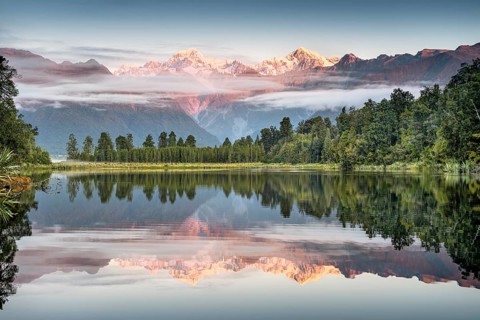 Veil clouds in front of Mount Cook and Mount Tasman are reflected in Lake Matheson in the evening light, Westland National Park