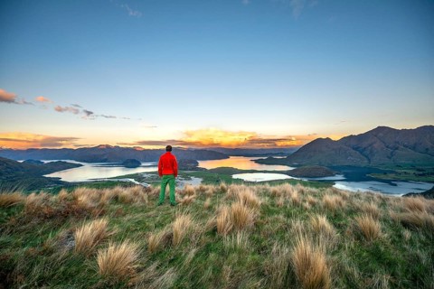 Walker looks out over Wanaka Lake and mountains at sunset, Rocky Peak