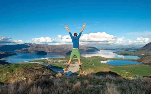 Hiker jumps in the air, view of Wanaka Lake and mountains