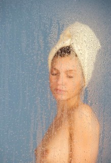 Woman sitting in a steam bath behind glass pane with drops of water, 24 years