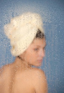 Woman sitting in a steam bath behind glass pane with drops of water, 24 years