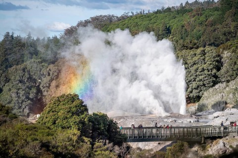 Tourists on bridge, view of erupting Pohutu Geyser with rainbow