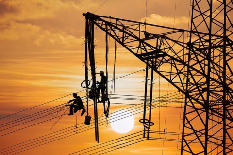 High voltage fitters working on the high voltage pylon at sunset, Baden-Wuerttemberg