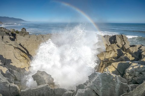 Blowhole with rainbow, splashing surf hole in the rock formations of Pancake Rocks