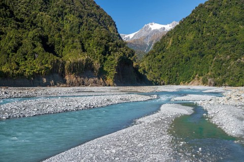 Gravel bed in the valley of the Karangarua River, forested slopes and glaciated peaks of New Zealand's Southern Alps