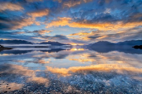Light beam of golden cloud atmosphere over Lake Te Anau, in the background mountain ranges of the Stuart Mountains and Franklin Mountains