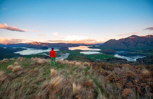Walker looks out over Wanaka Lake and mountains at sunset, Rocky Peak