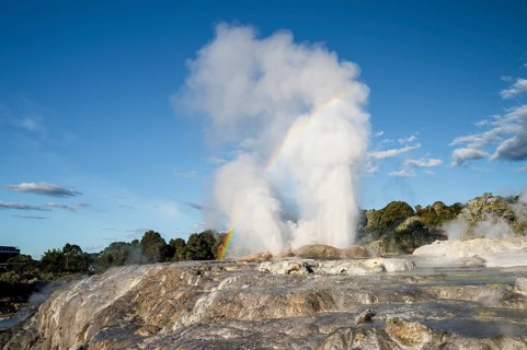 Erupting Pohutu Geyser with rainbow, sinter terraces