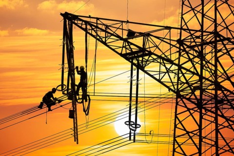 High voltage fitters working on the high voltage pylon at sunset, Baden-Wuerttemberg