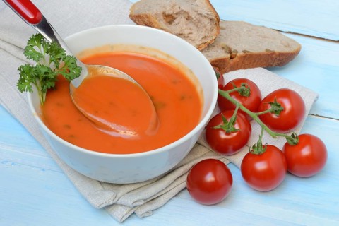 Tomato soup with spoon in bowl, tomatoes
