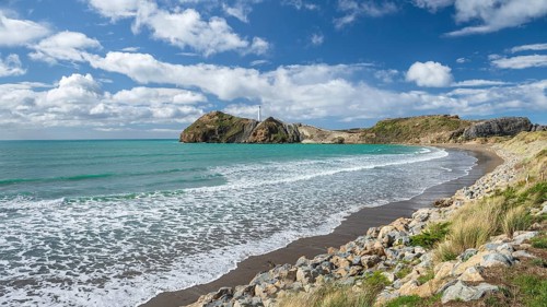 Beach with turquoise sea, in the back lighthouse of Castlepoint