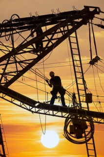 High voltage fitters working on the high voltage pylon at sunset, Baden-Wuerttemberg