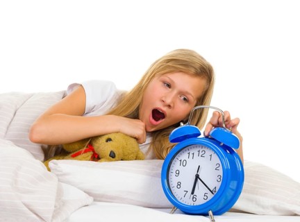 Girl in bed yawns when alarm clock rings