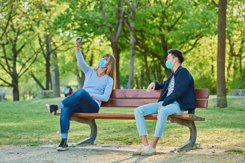 Man and woman wearing a face mask on a park bench in a municipal park